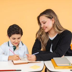 One-on-one tutor helping a young student write in his notebook at a study table